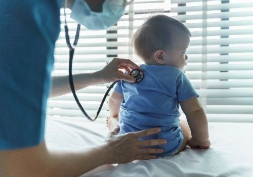 Doctor holding stethoscope on crawling baby
